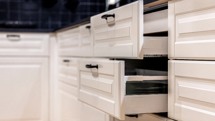 Modern traditional off-white kitchen base cabinets featuring open drawers that demonstrate internal storage capacity and dark pull handles.